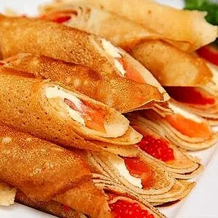 Close-up of three crispy crepes filled with cream, slices of smoked salmon, and garnished with red caviar.