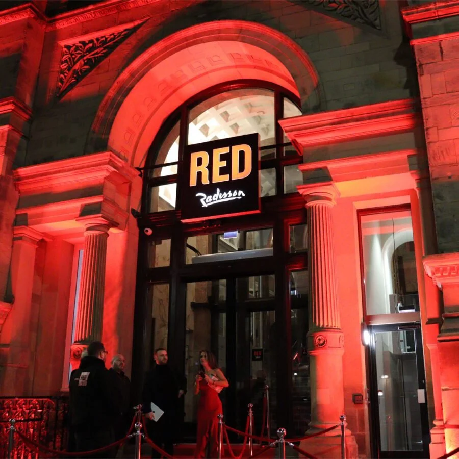 The entrance of Radisson hotel, illuminated with red lighting, showcasing a grand arch with columns and a sign that reads 'RED Radisson'.