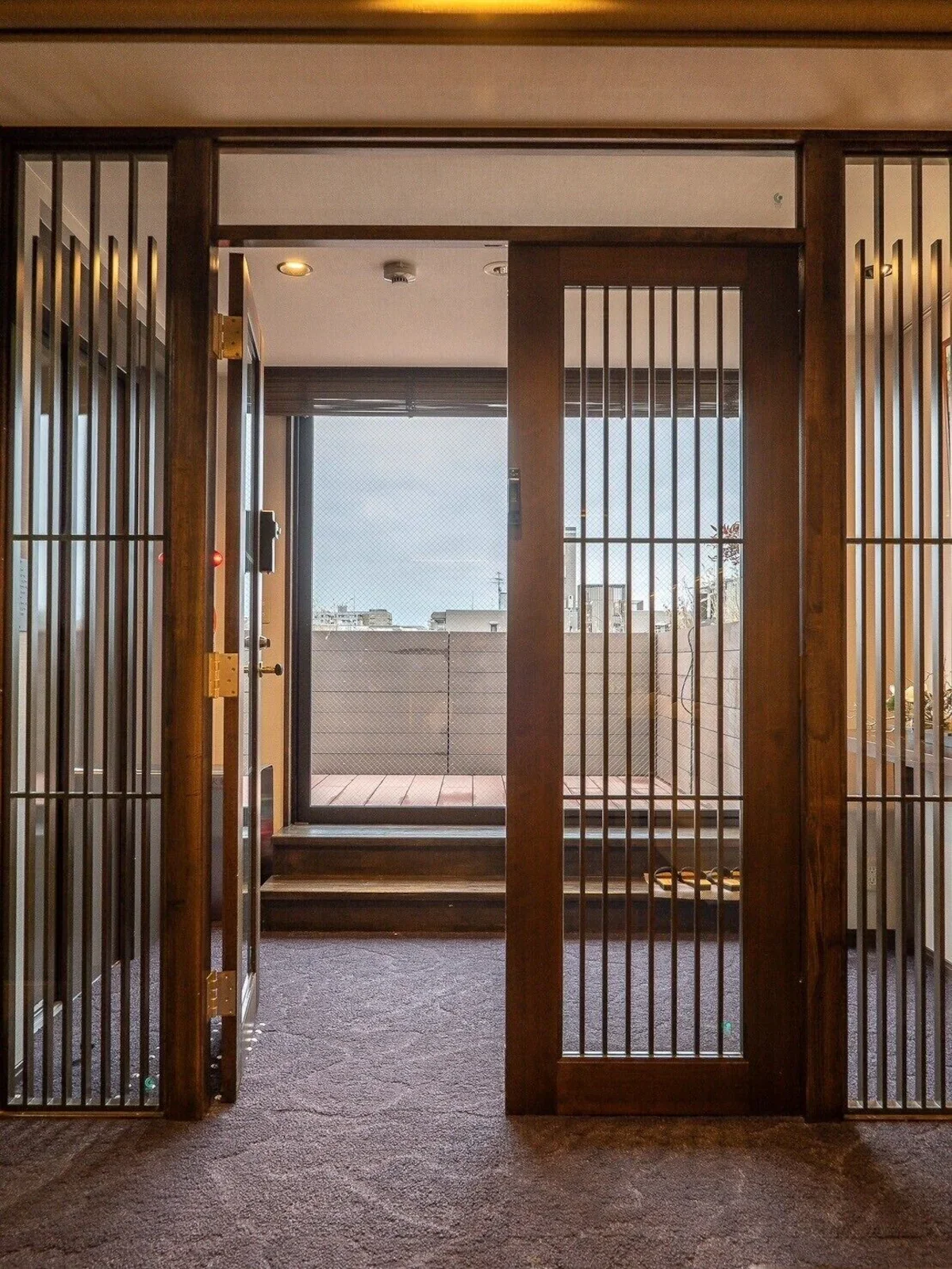 Indoor sliding door with wooden frame and bars leading to a balcony with a city view.