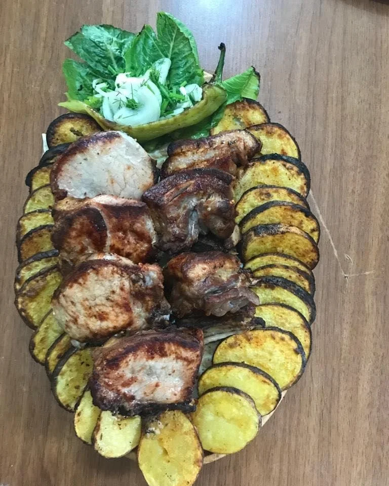 Grilled chicken thighs, sliced roasted eggplant, and a small salad with greens in a bowl at the top on a wooden table.