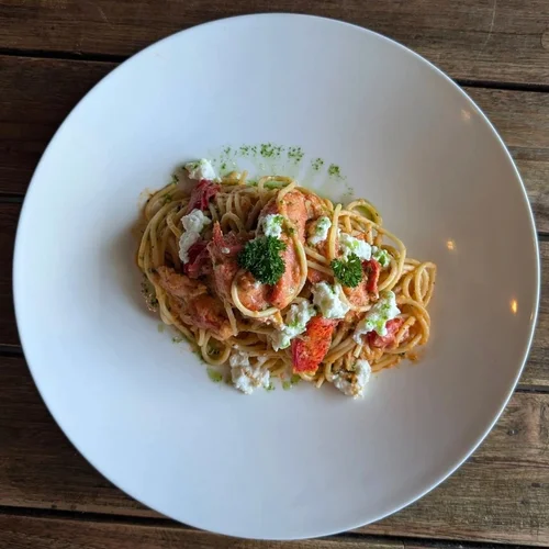 A white plate of pasta with red and green sauce, garnished with fresh herbs, on a wooden table.