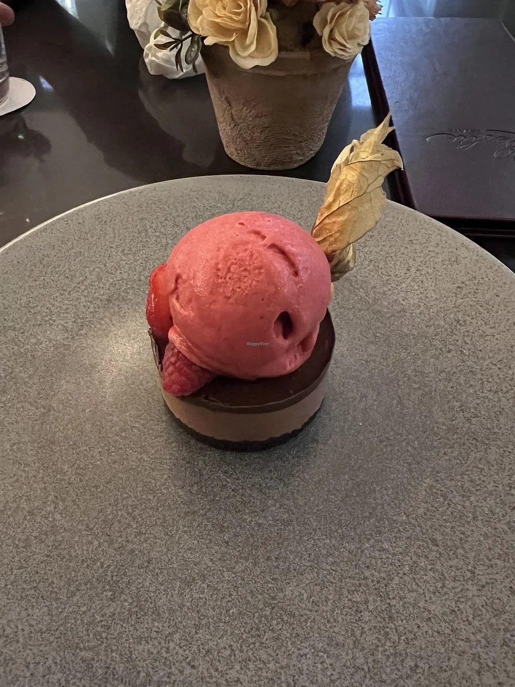 Dessert with a scoop of pink ice cream and a piece of dried leaf decoration on top, served on a gray plate.