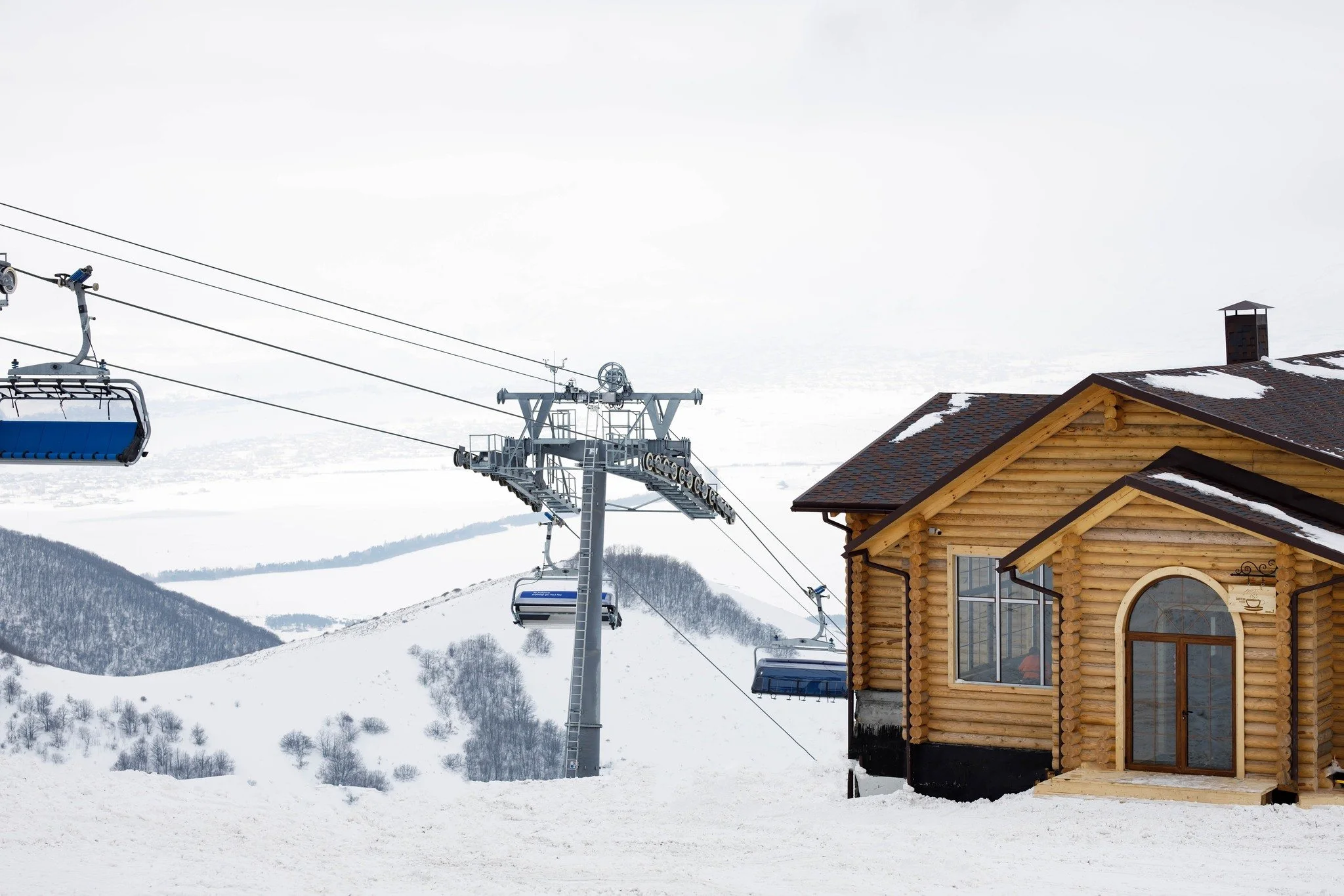 Snow-covered mountain landscape with ski lift chairs and a wooden cabin.