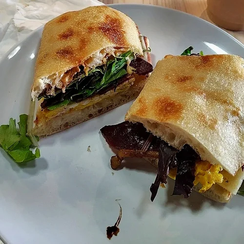 Two halves of sandwiches with toasted bread, lettuce, meat, and scrambled eggs on a white plate