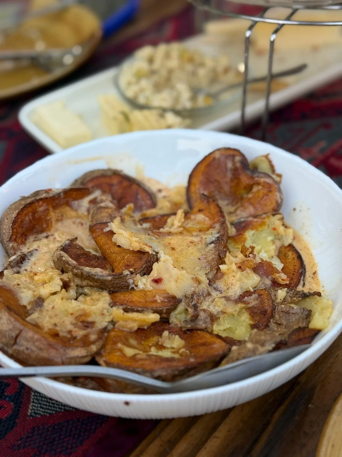 Sweet potato casserole with marshmallows in a white bowl, with cheese and other food items in the background.