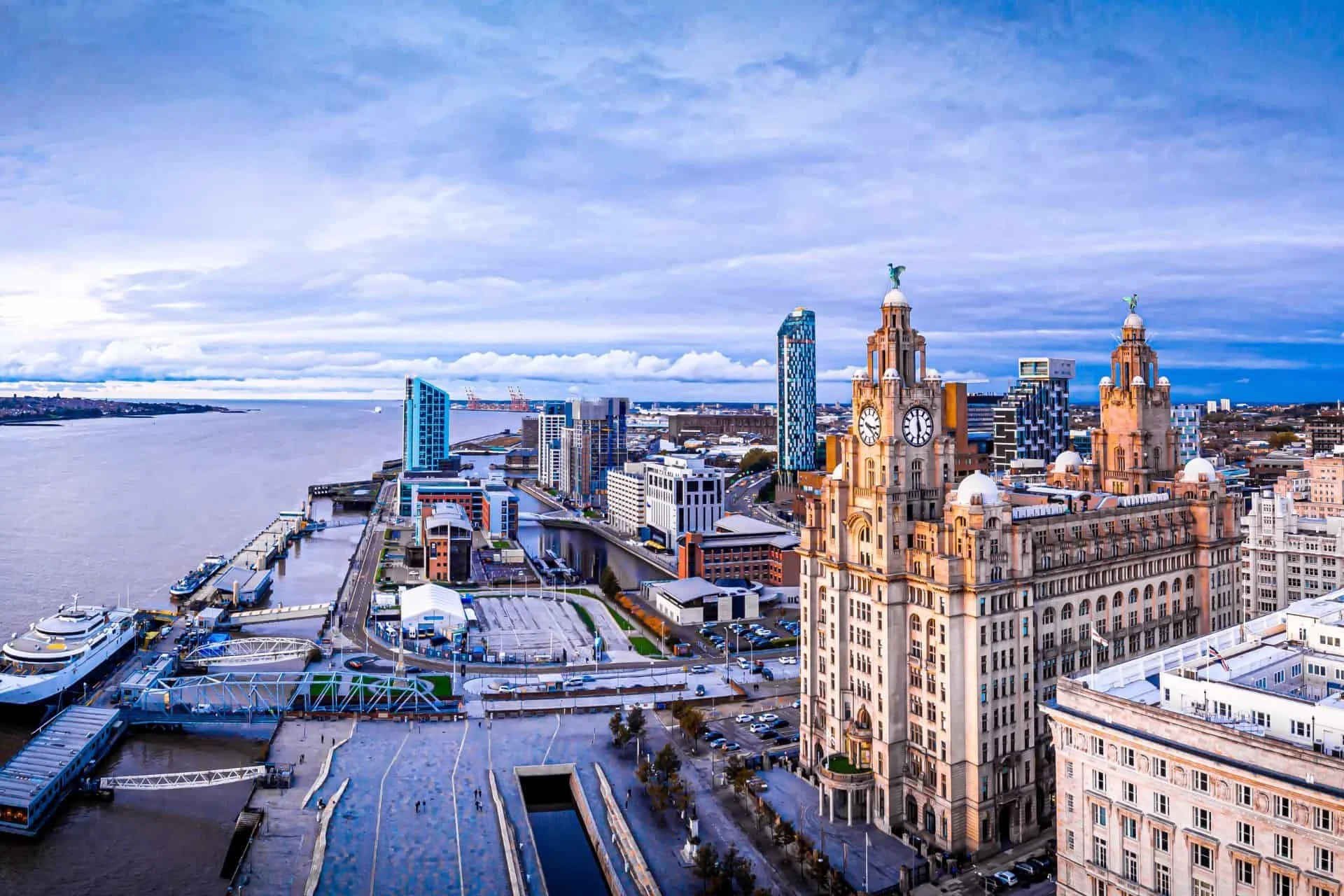 Aerial view of a city skyline by a river with historic and modern buildings under a cloudy sky.