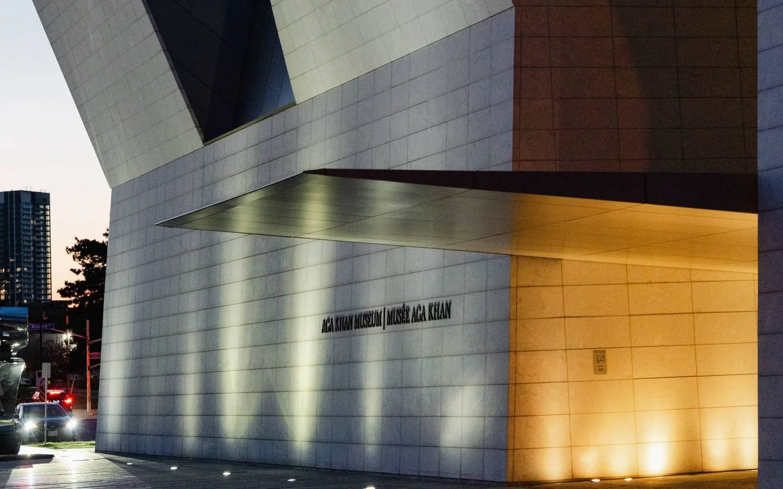 Exterior view of the Aga Khan Museum building at dusk, with modern architecture featuring white tiled walls and soft lighting.