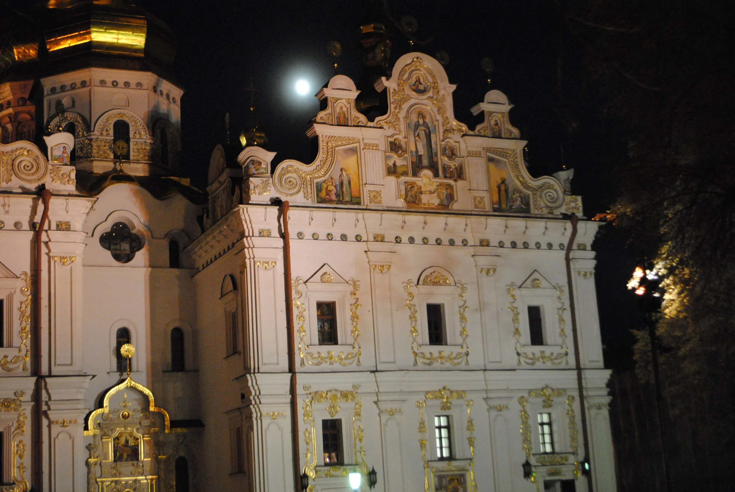 Nighttime view of a decorated church with gold accents and religious paintings, illuminated by external lights and moonlight.
