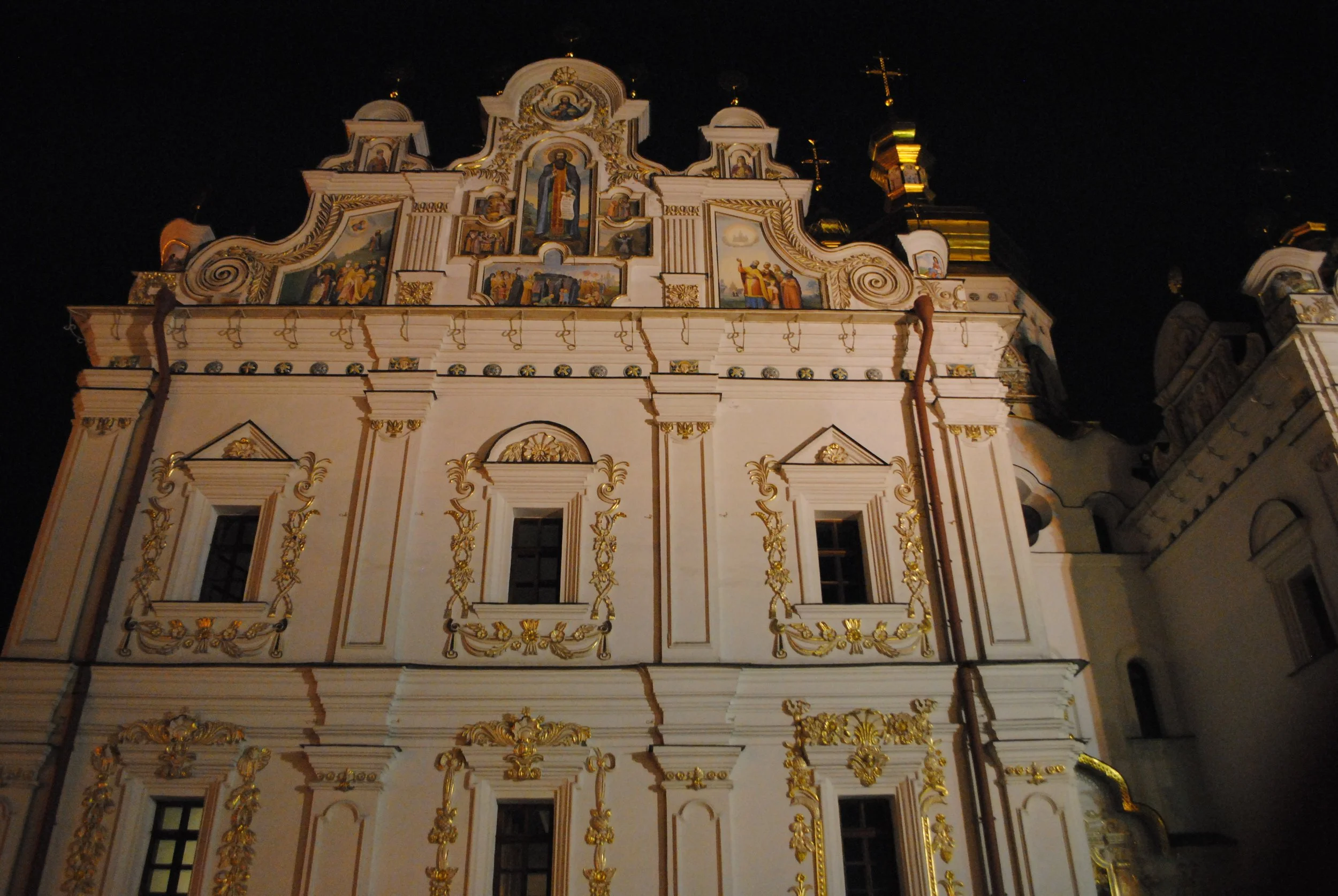 Night view of a historic Baroque-style church with ornate details and religious paintings on its facade, illuminated at night.