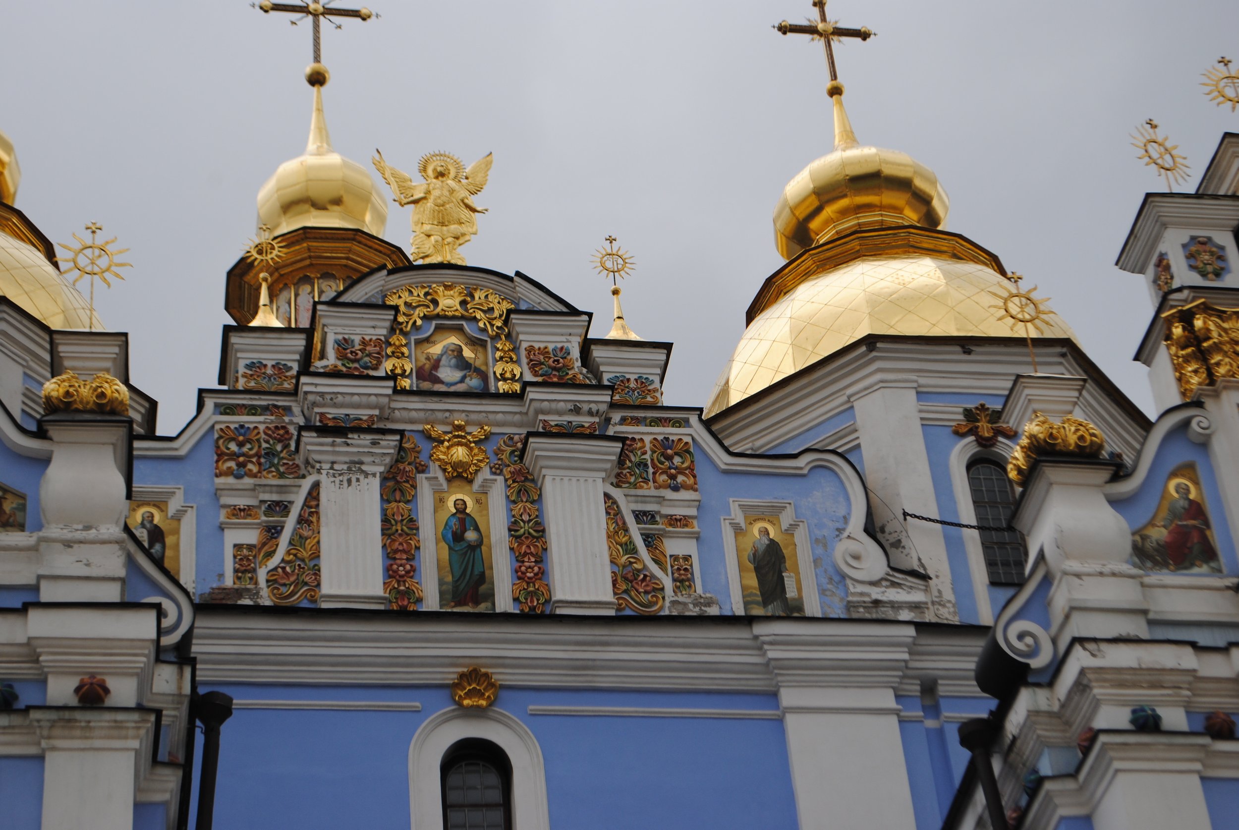 The image shows the ornate roof of a church with golden domes and crosses, decorative painted icons, and architectural details.
