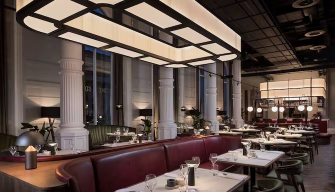 Elegant restaurant dining area with white columns, large windows, and modern lighting fixtures, set with tables and glassware.