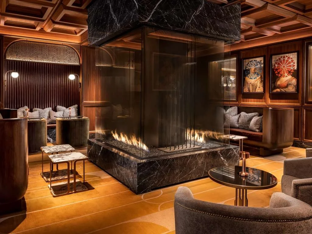 Luxury hotel lounge with a modern fireplace, dark wood paneling, and artwork on the walls.