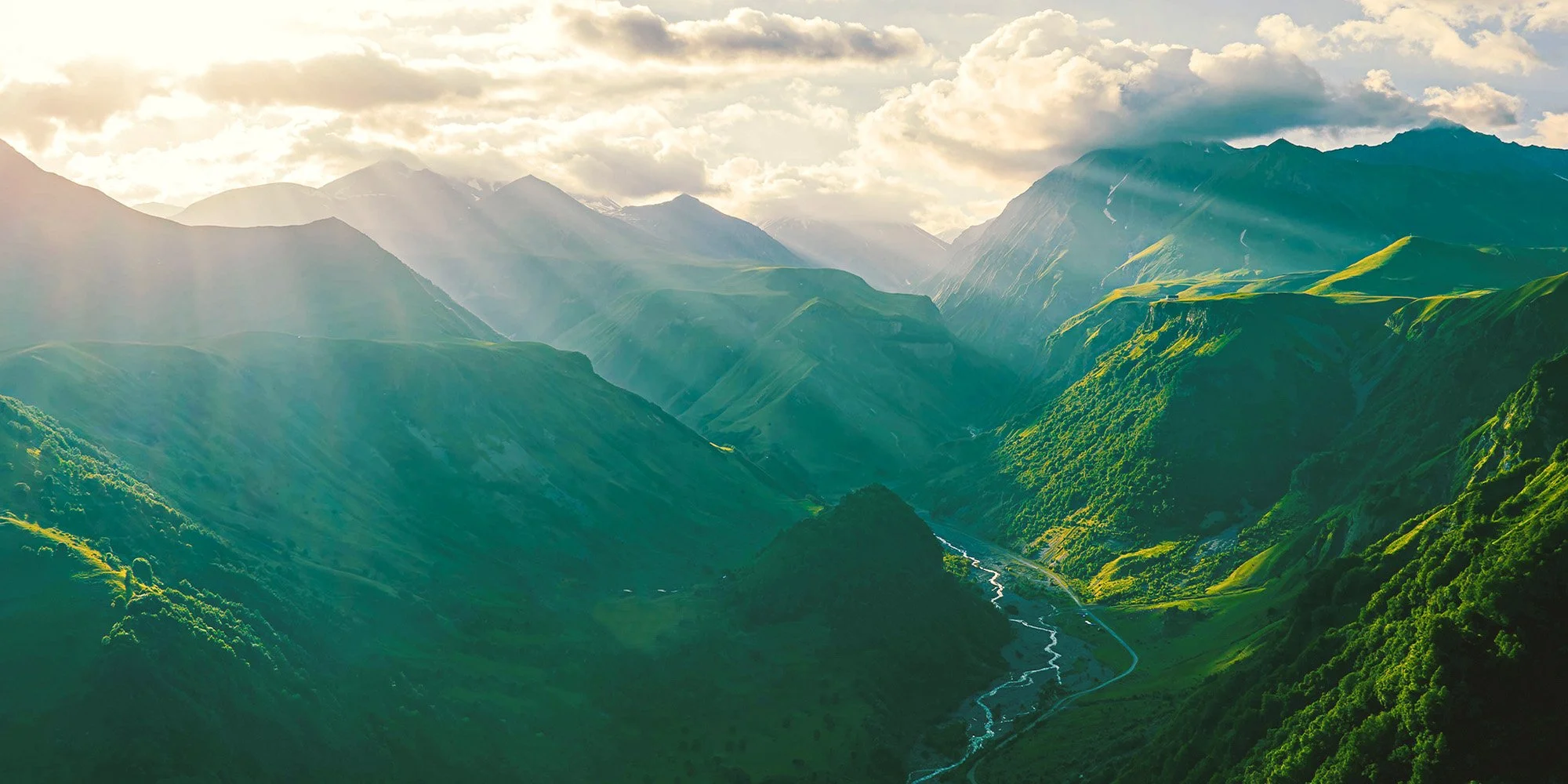 Sunlight shining over lush green mountains with a river flowing through the valley.