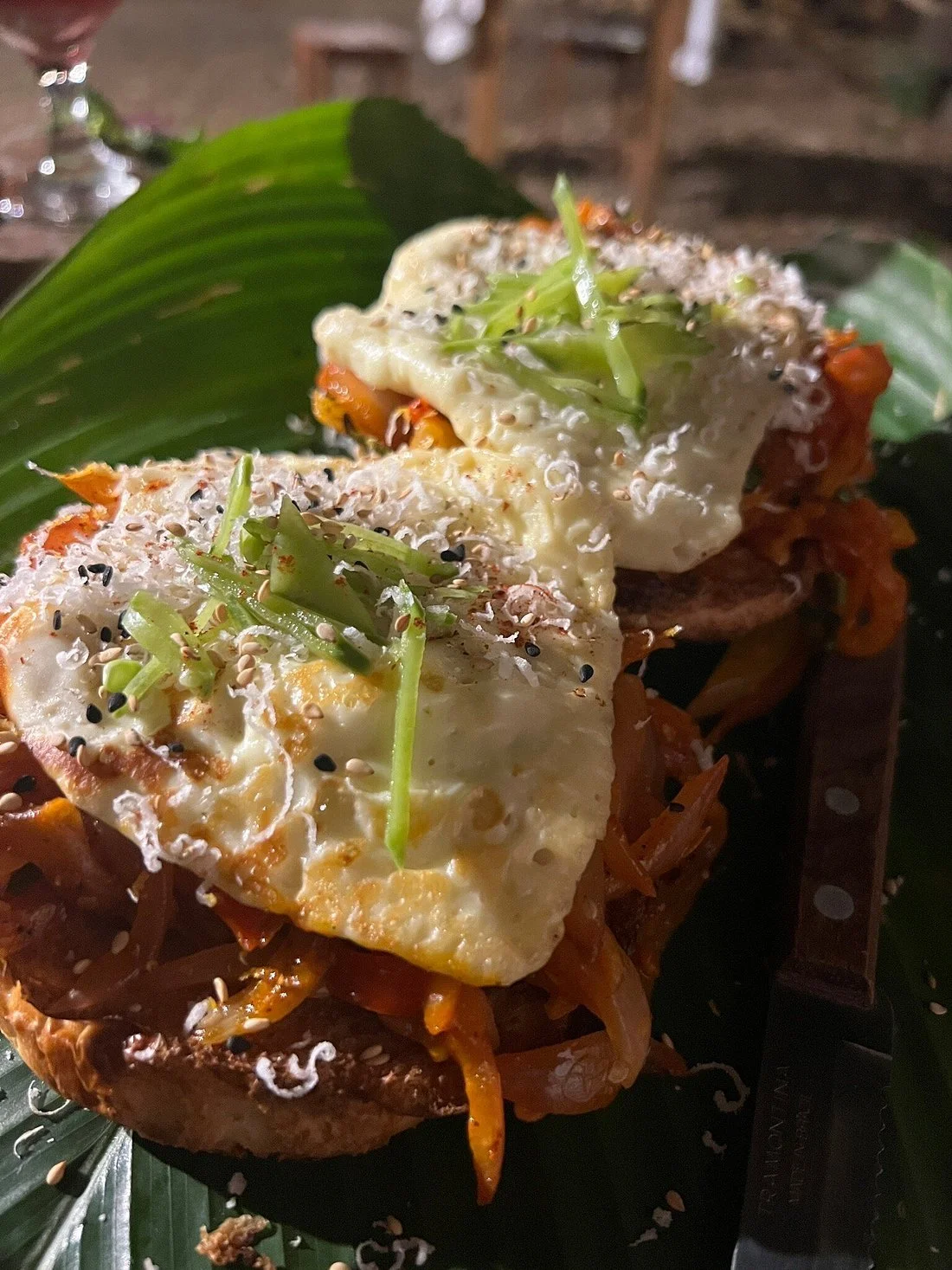 Two fried eggs topped with sprouts, sesame seeds, and black pepper, served over a bed of shredded vegetables on a banana leaf.