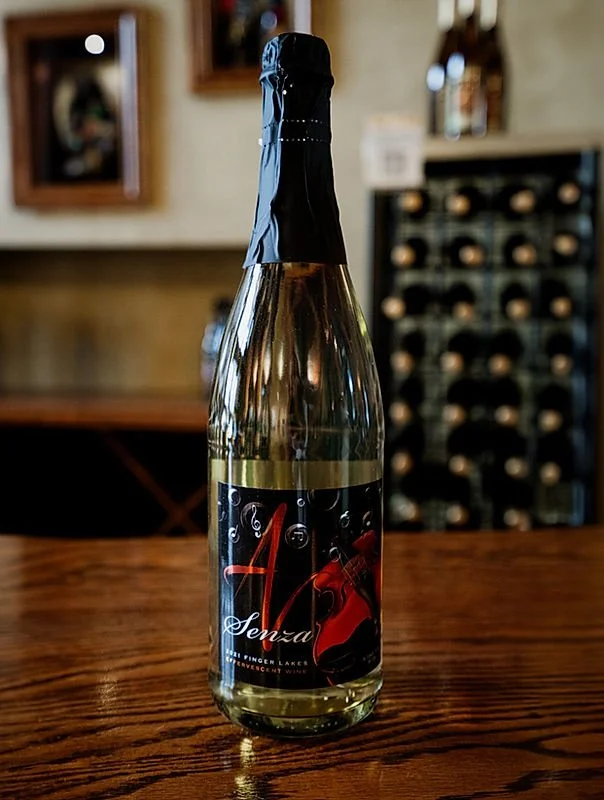 A bottle of sparkling wine or champagne with a black foil cover on a wooden table in a restaurant or bar setting.