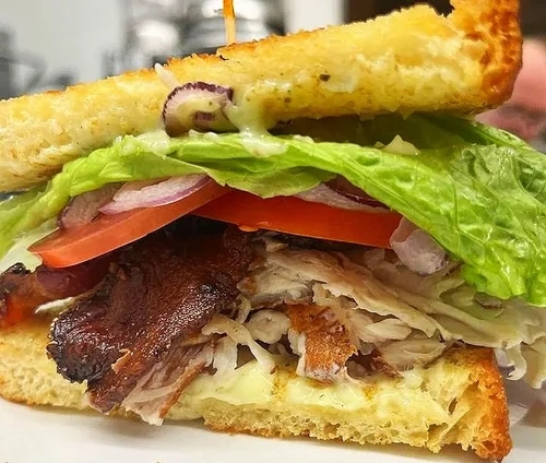 Close-up of a sandwich with lettuce, tomato, bacon, turkey, melted cheese, and toasted bread.