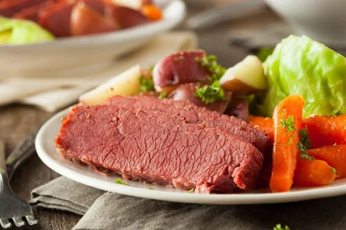 Cooked slices of medium-rare roast beef served with roasted carrots, potatoes, and a side of leafy lettuce.
