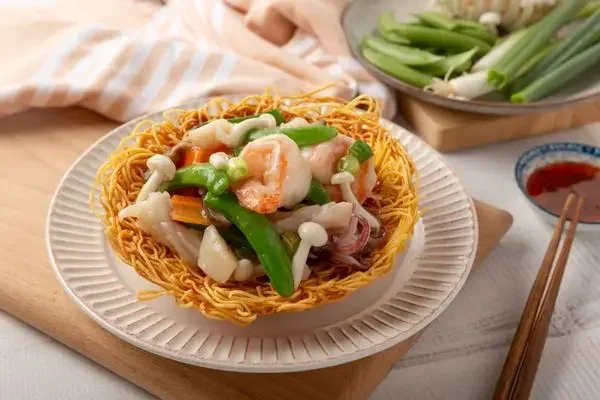 A bowl of crispy fried noodles topped with shrimp, green bell peppers, and white mushrooms