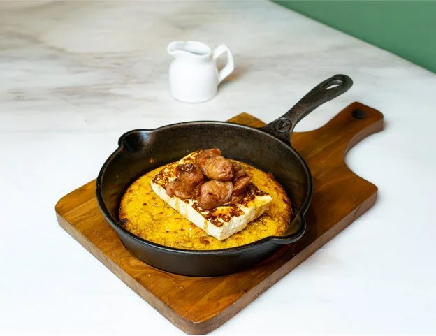 Fried dish with meat on top, served on a piece of toast inside a cast iron skillet, placed on a wooden board.