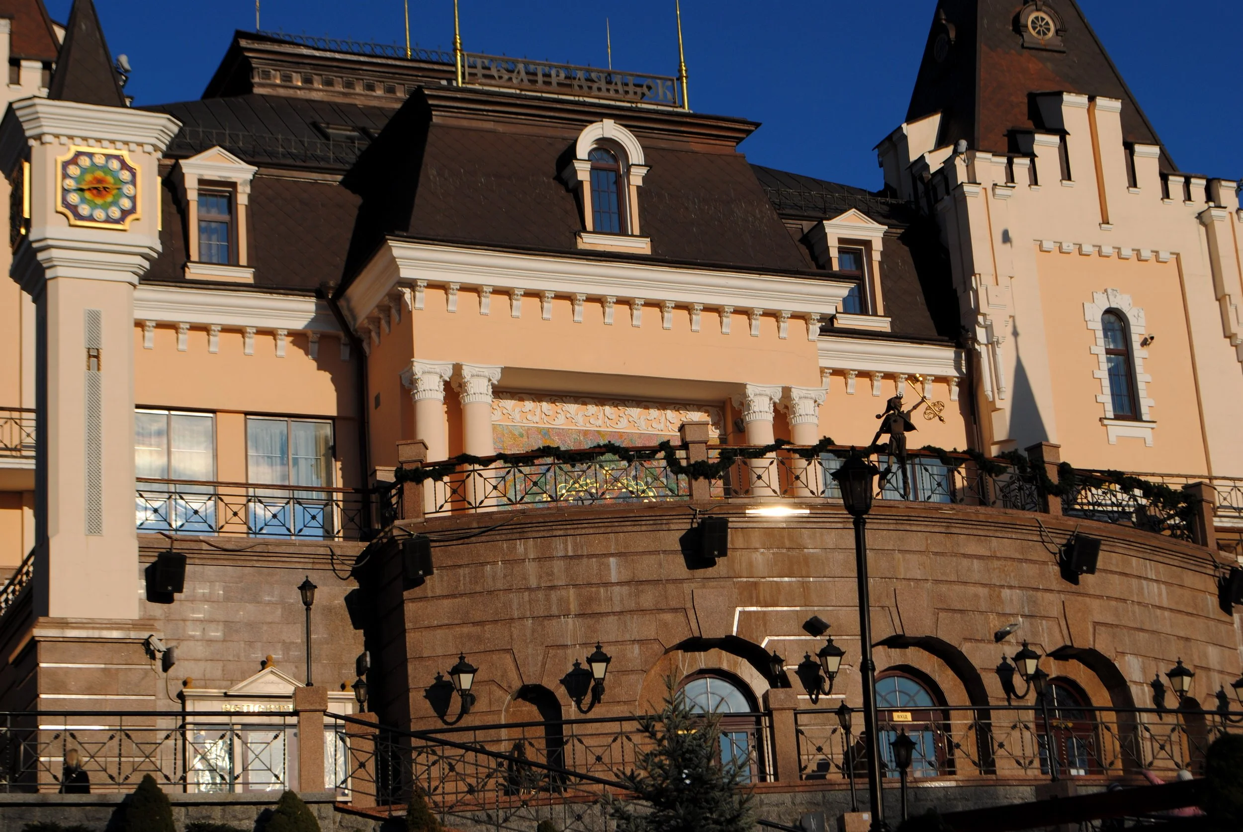 Close-up of a historic building with decorative architecture, towers, and a sign in Cyrillic at the top, under a clear blue sky.