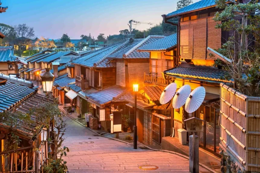 Traditional Japanese street at dusk with wooden buildings, paper lanterns, and umbrellas.