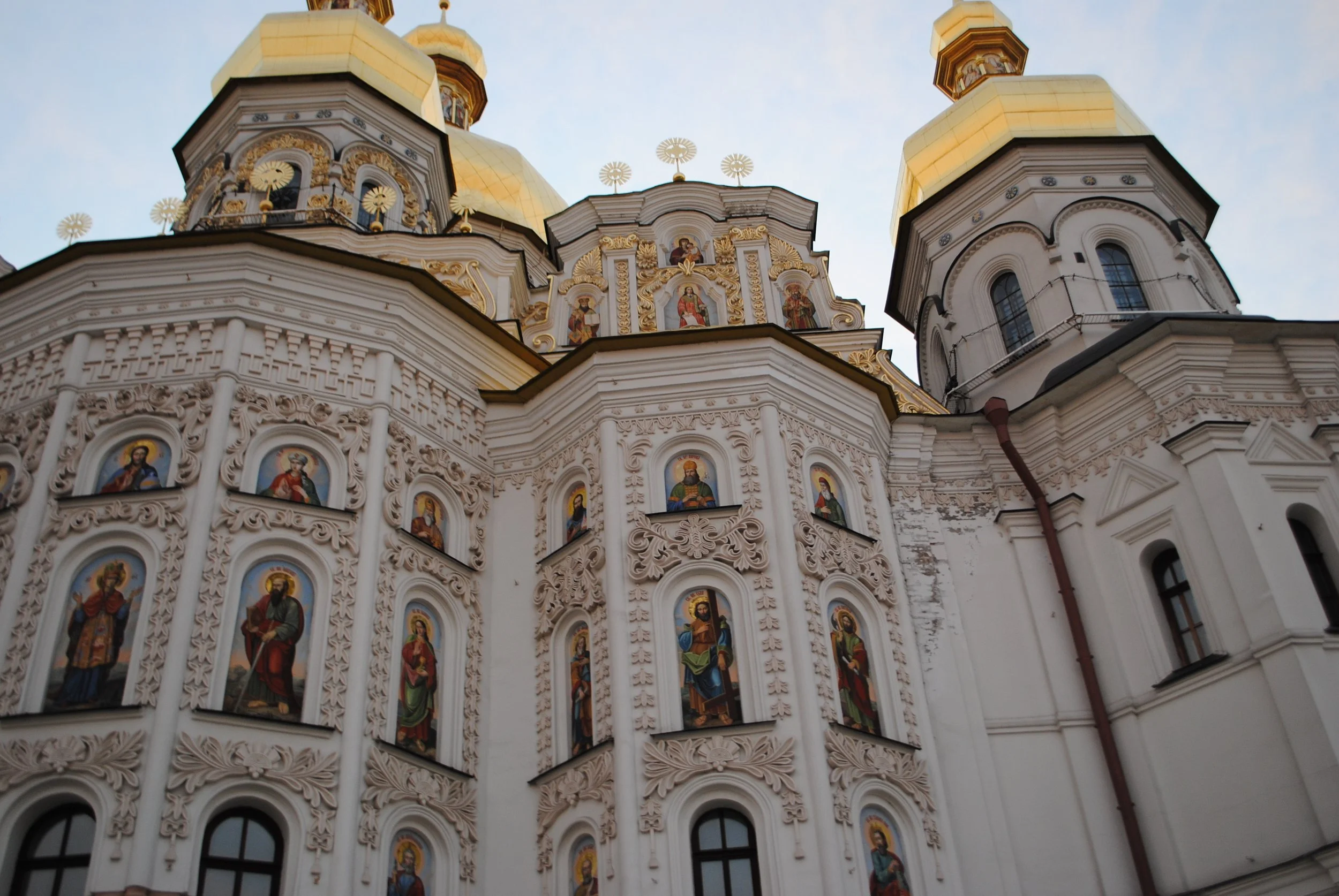 A close-up view of a church with ornate white walls and golden domes, featuring religious icons in colorful frames.