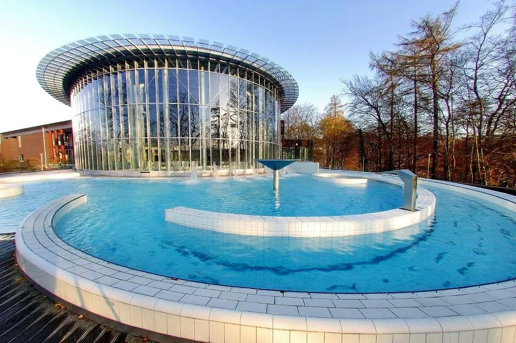 A modern building with large glass windows surrounded by a circular pool and leafless trees in the background.