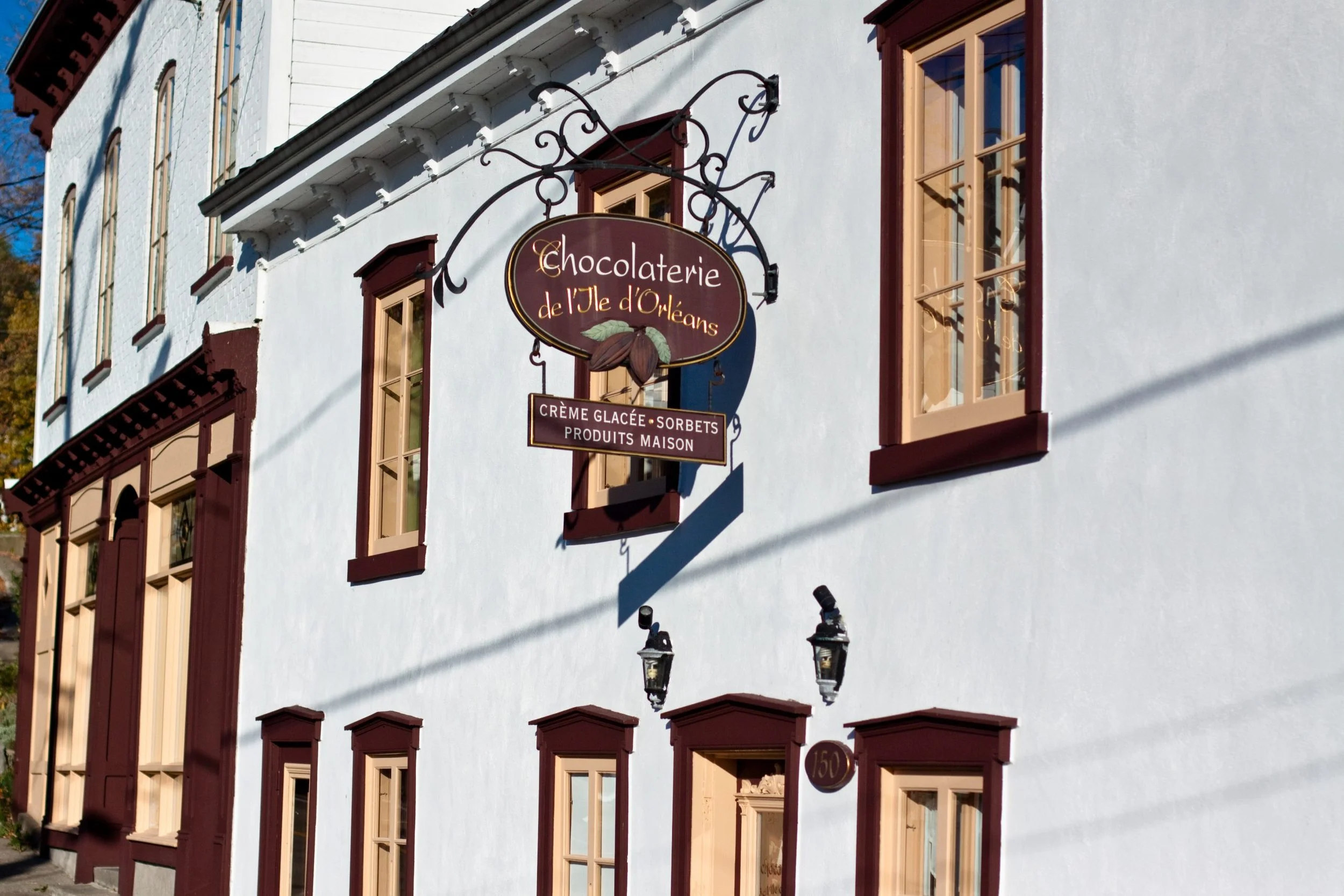 Exterior of a white building with maroon trim, displaying a sign for Chocolaterie de l'Ile d'Orléans, offering ice cream, sorbets, and homemade products.