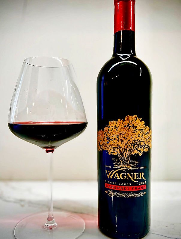A bottle of 2021 Wagner Cabernet Franc wine from Lake Oak Vineyard next to a glass of red wine on a white surface with a plain background.
