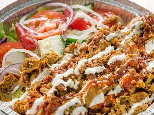 Tray of food with shredded meat, white sauce, and vegetables including tomatoes, onions, and cucumber slices.