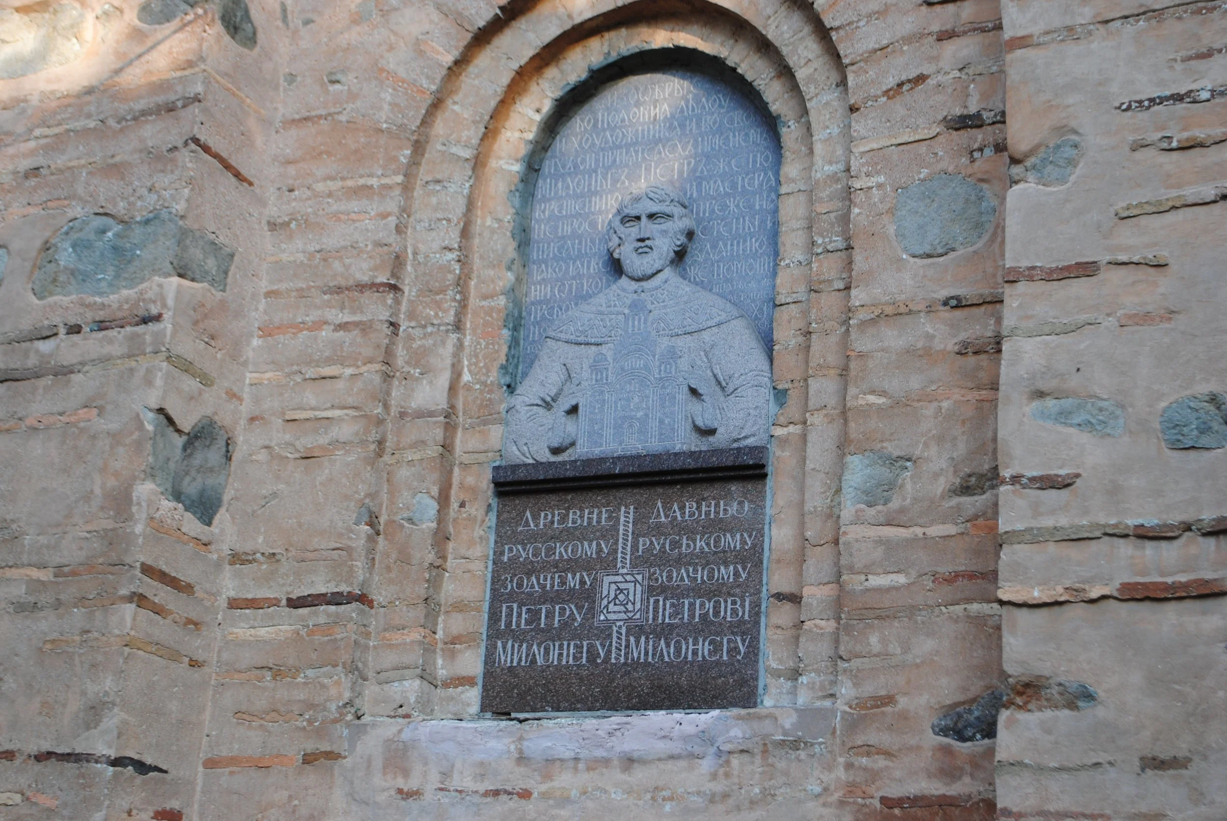 A stone plaque with carved portrait of a historical figure, surrounded by inscriptions in a Cyrillic script, mounted on an old brick wall.
