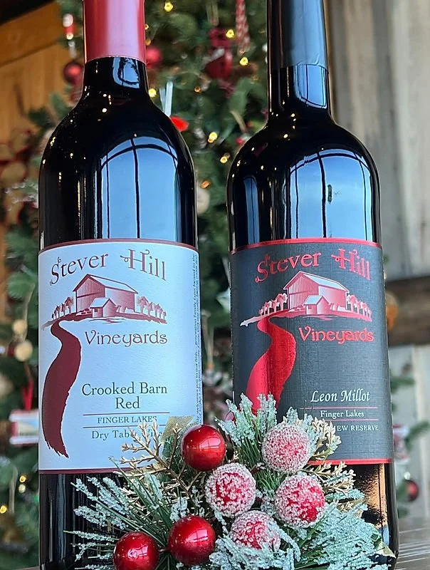 Two bottles of Steven Hill Vineyards wine placed in front of a decorated Christmas tree, with holiday ornaments and frosted pine branches.