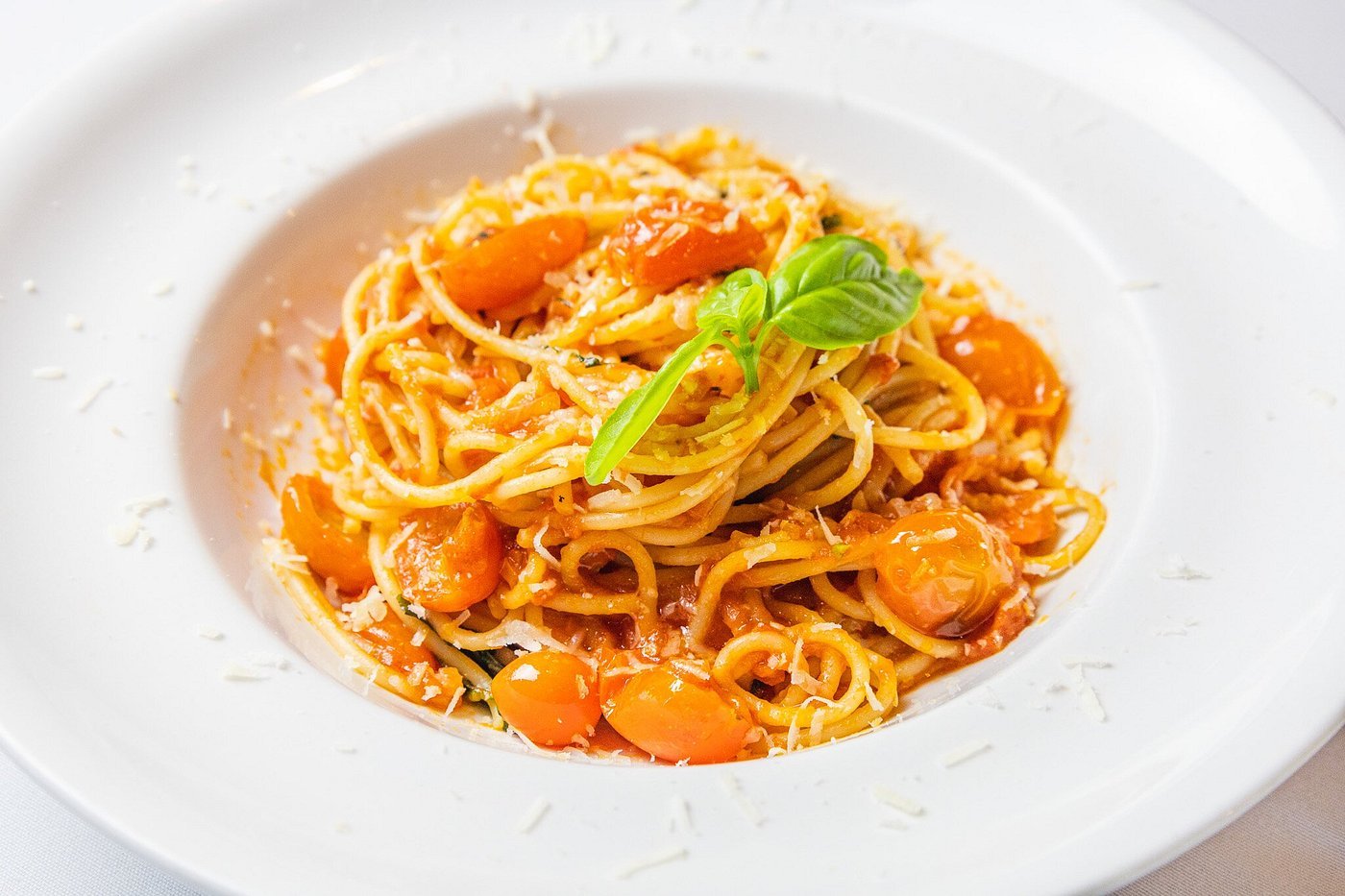 Plate of spaghetti with cherry tomatoes, grated cheese, and fresh basil garnish.