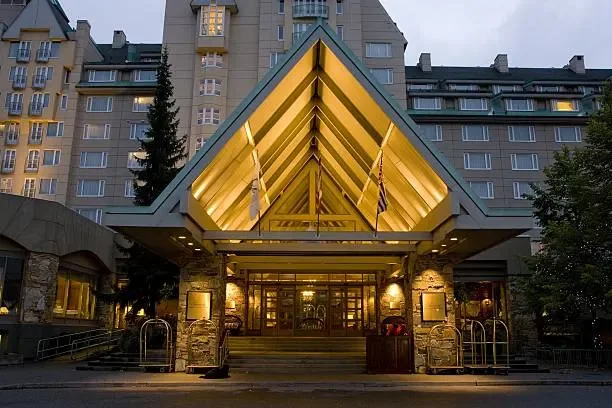 Entrance of the Sofitel hotel with a security guard standing at the front in a suit and hat, illuminated signage, glass doors, and a staircase leading up to the entrance.