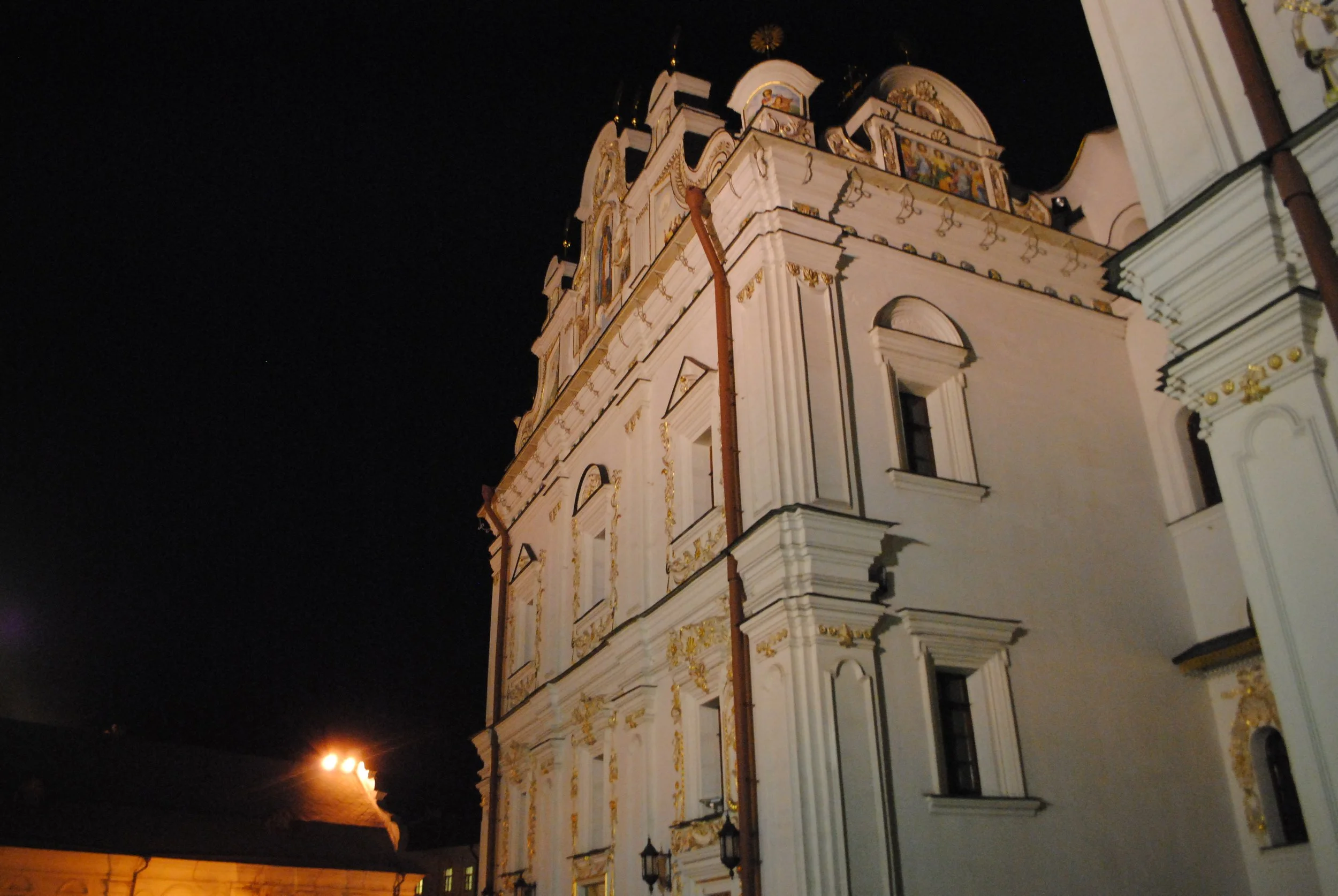 Nighttime view of a white ornate church with gold accents and decorative paintings on the upper walls.