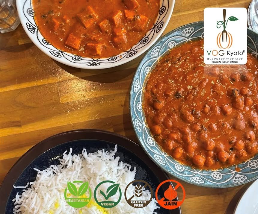 Two bowls of Indian-style curry with chickpeas and vegetables, and a plate of white rice on a wooden table.