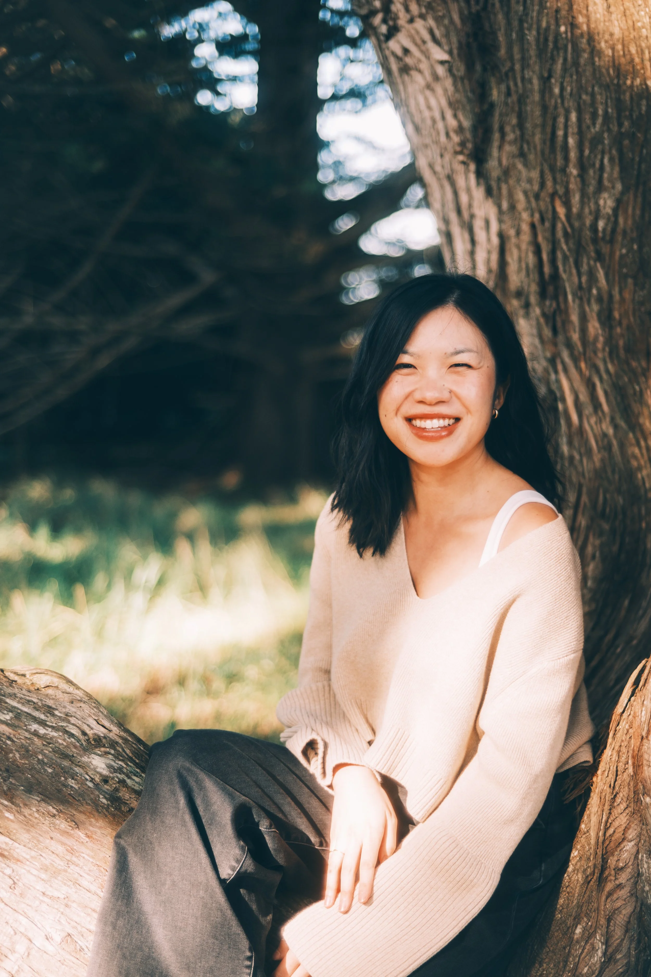 Woman sitting on a tree who is an artist posing for a photo who is happy.