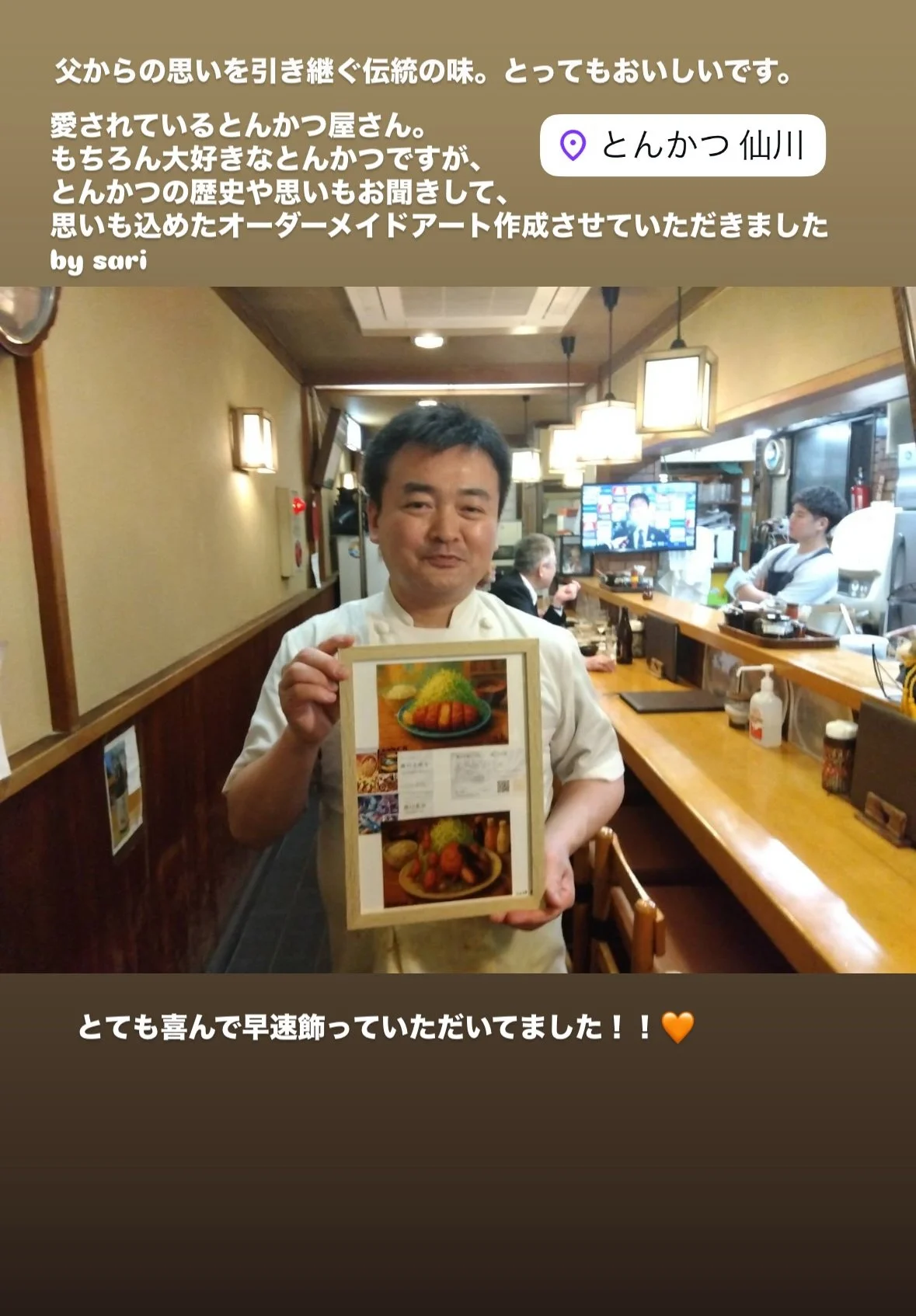A man dressed as a chef holding a framed picture of a dish with rice, vegetables, and fried items inside a restaurant with wood-paneled walls and hanging lamps.