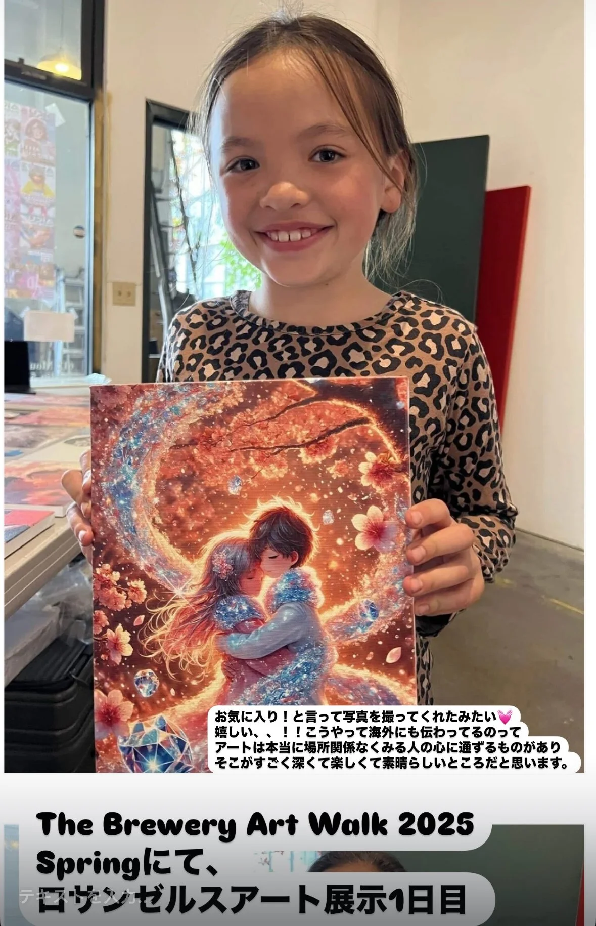 A young girl with a big smile holding a colorful art print of an anime-style couple embracing, surrounded by glowing and floral effects, in a room with a window and art supplies.