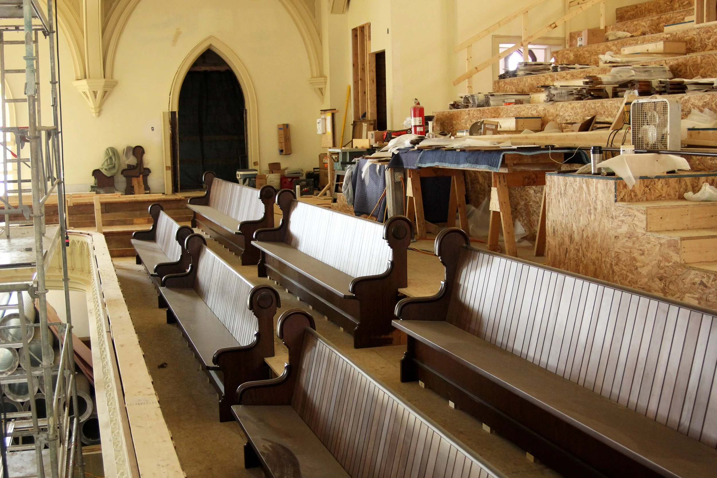 Medium brown wooden pews with rounded and trim detailing on the arm rests and panel detailing on the back rests.