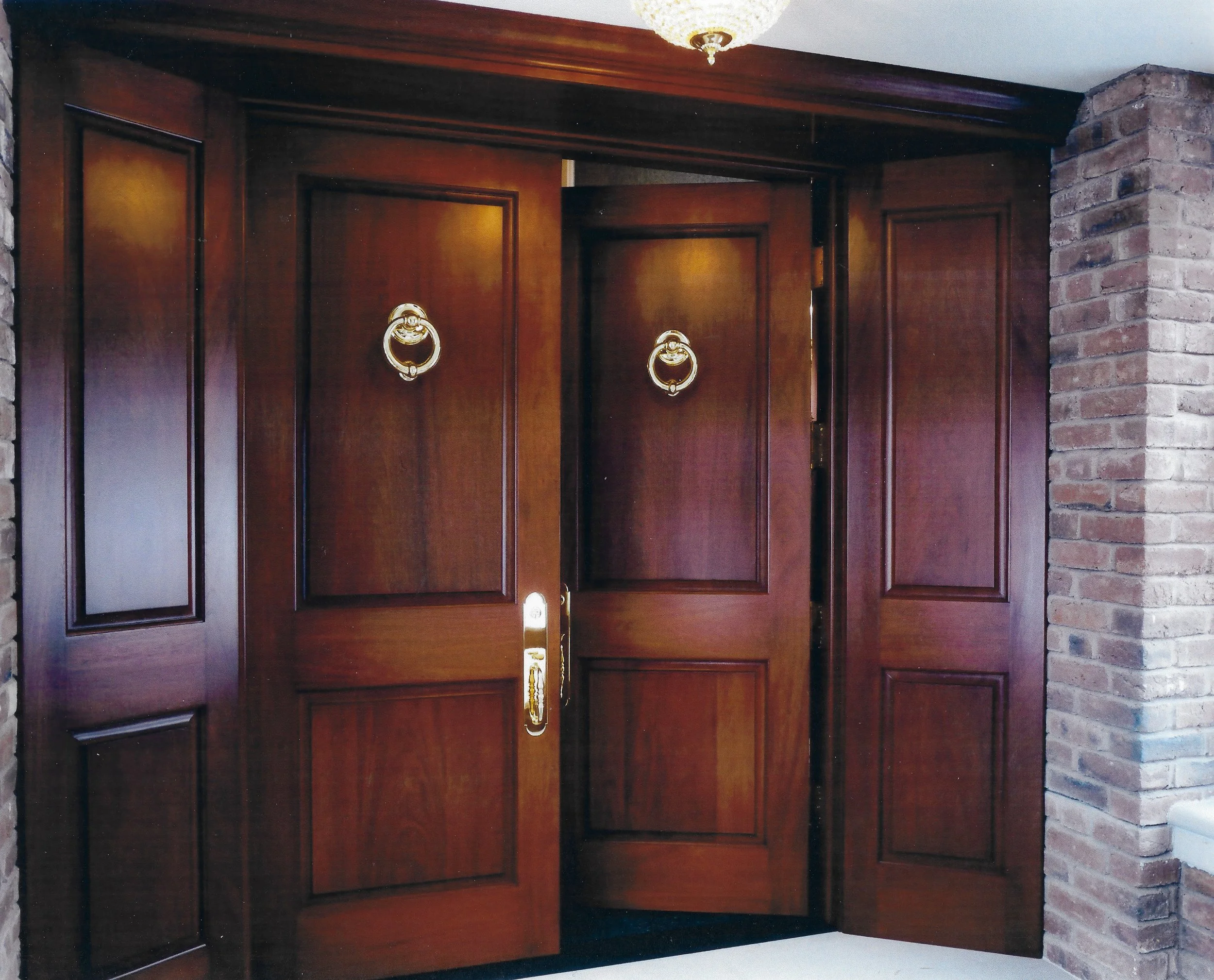 Large dark brown mahogany wooden entryway doors with inset trim detailing and large gold door knockers and handles.