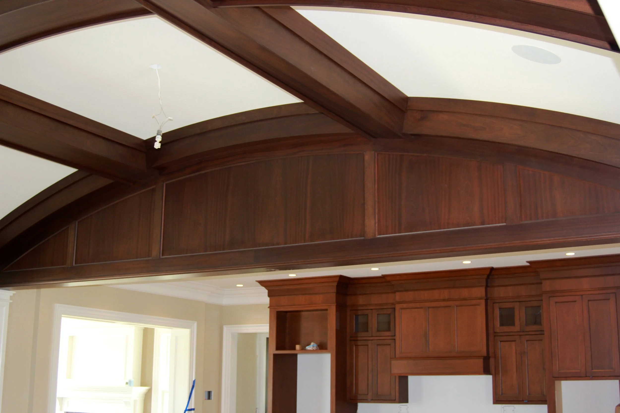 Close up on dark brown wooden barrel vault coffered ceiling with inset panels, with the top set of dark brown wooden custom built-in kitchen cabinetry in the background.