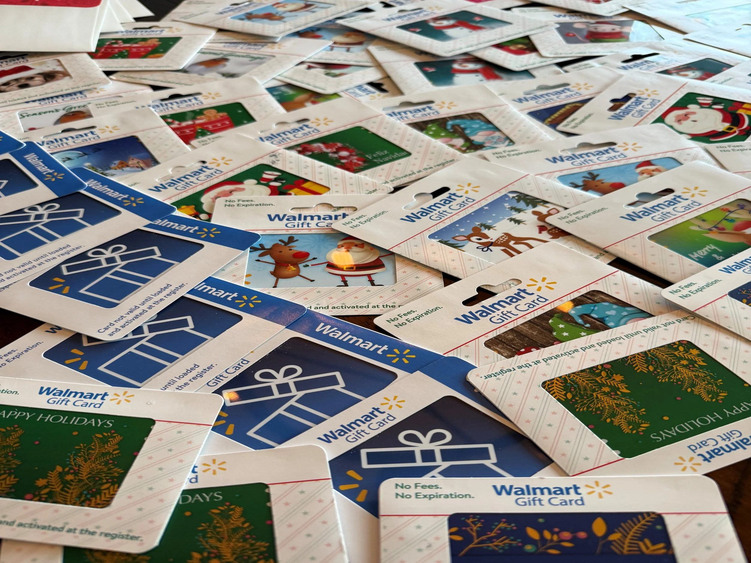 A large pile of Walmart gift cards with Christmas-themed and generic designs scattered across a surface.
