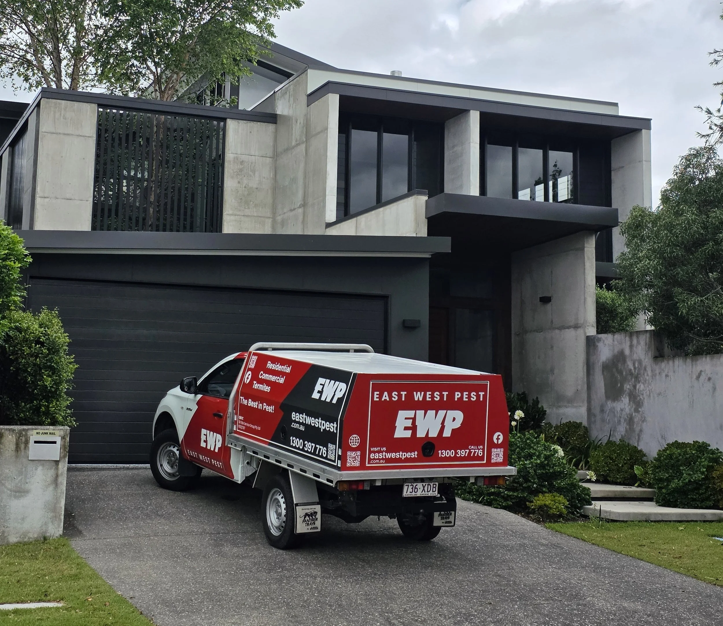A modern multi-story home with concrete and glass design and the East West Pest control truck parked outside during a professional Ipswich pest control service.
