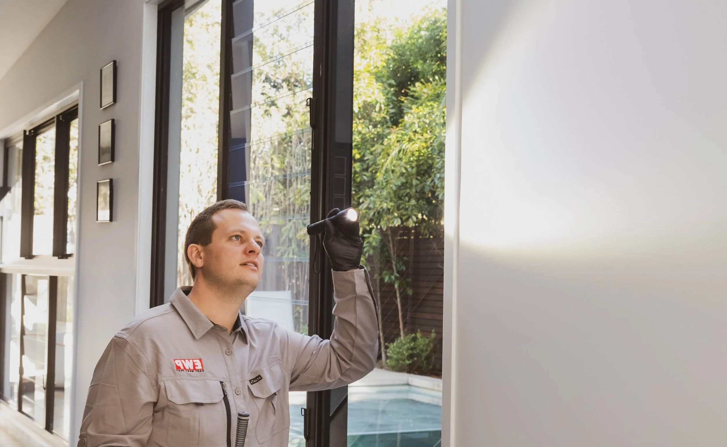 Termite inspection inside a Brisbane home with technician using a torch to check internal wall for signs of termite activity.