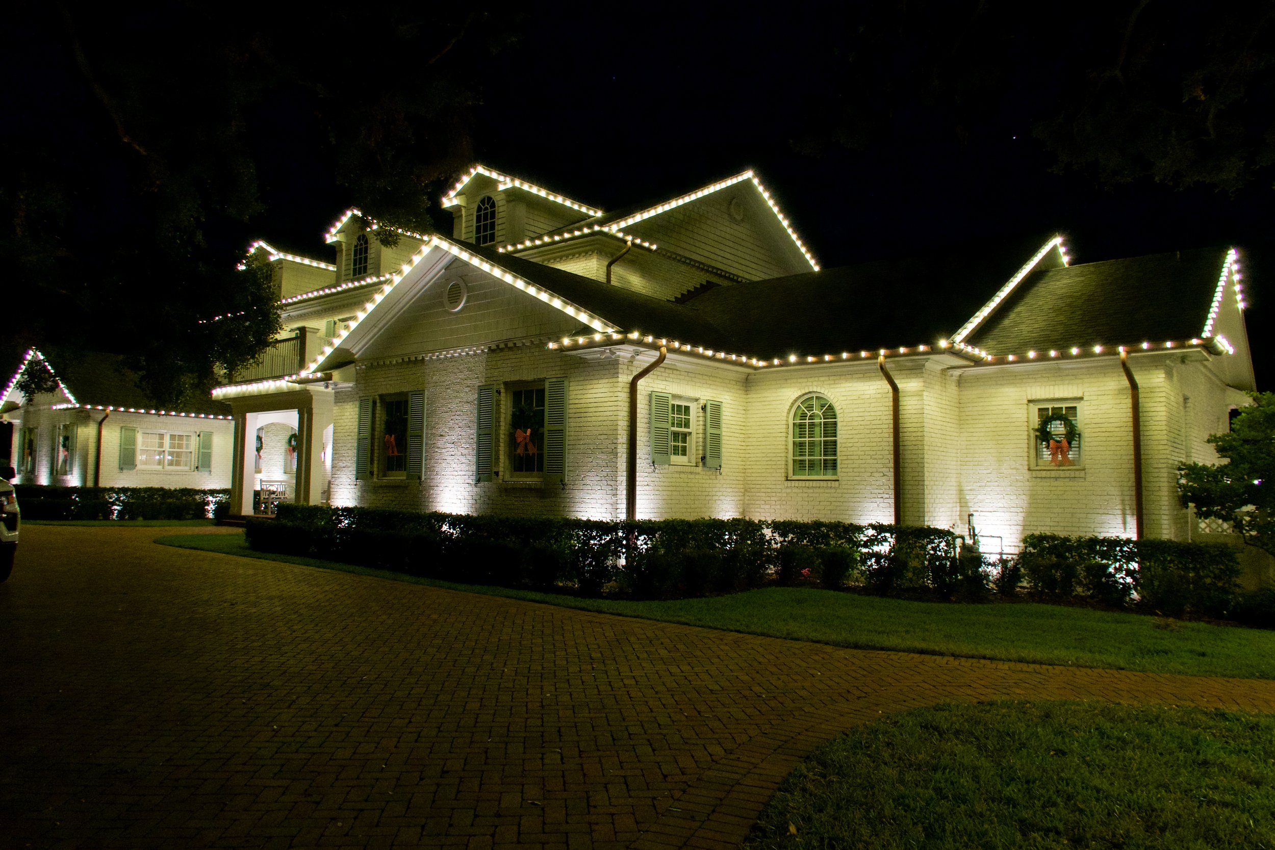 A white brick house decorated with white string lights outlining the roof at night.
