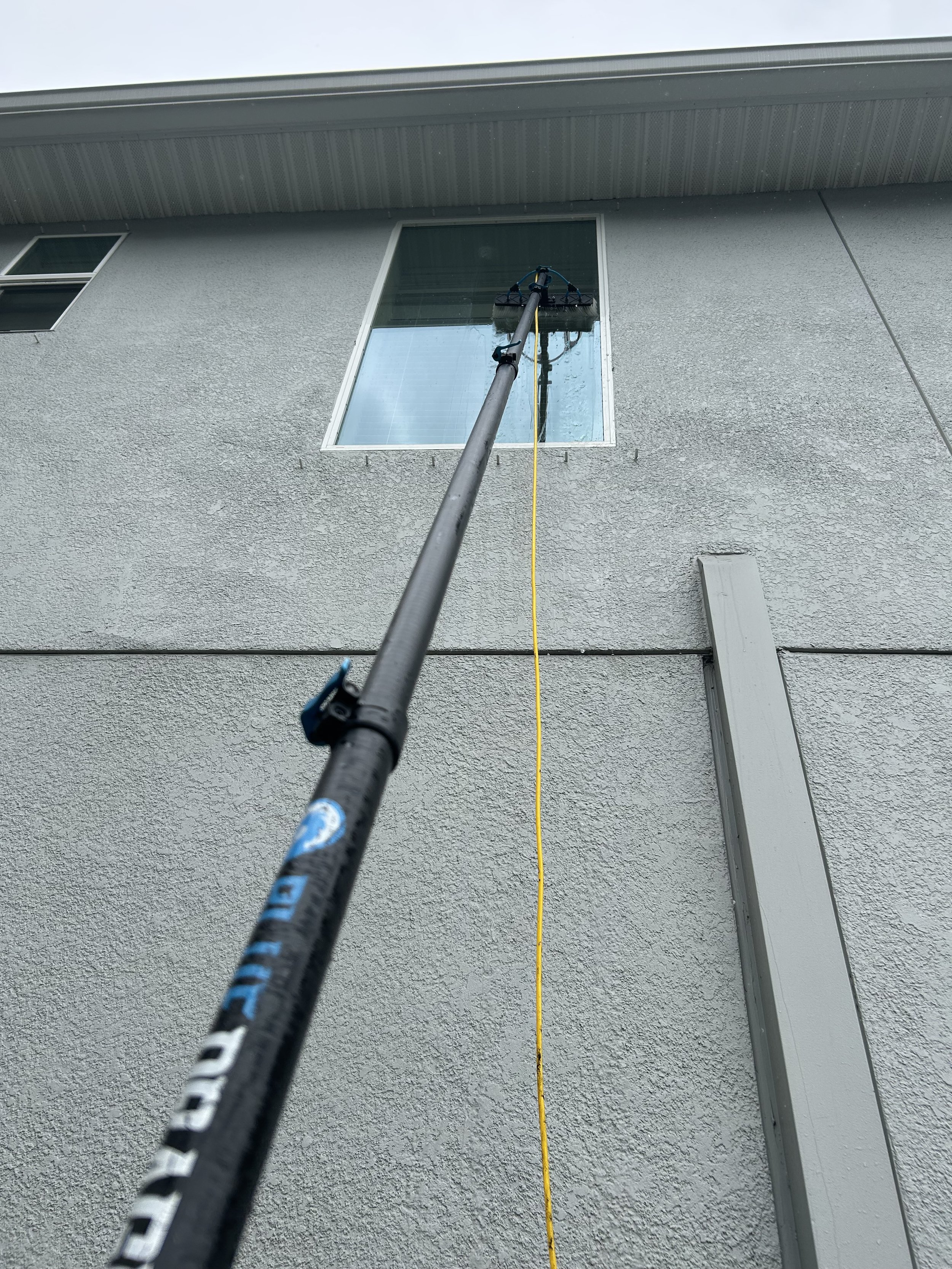 Window cleaning pole reaching a high window of a gray stucco building.