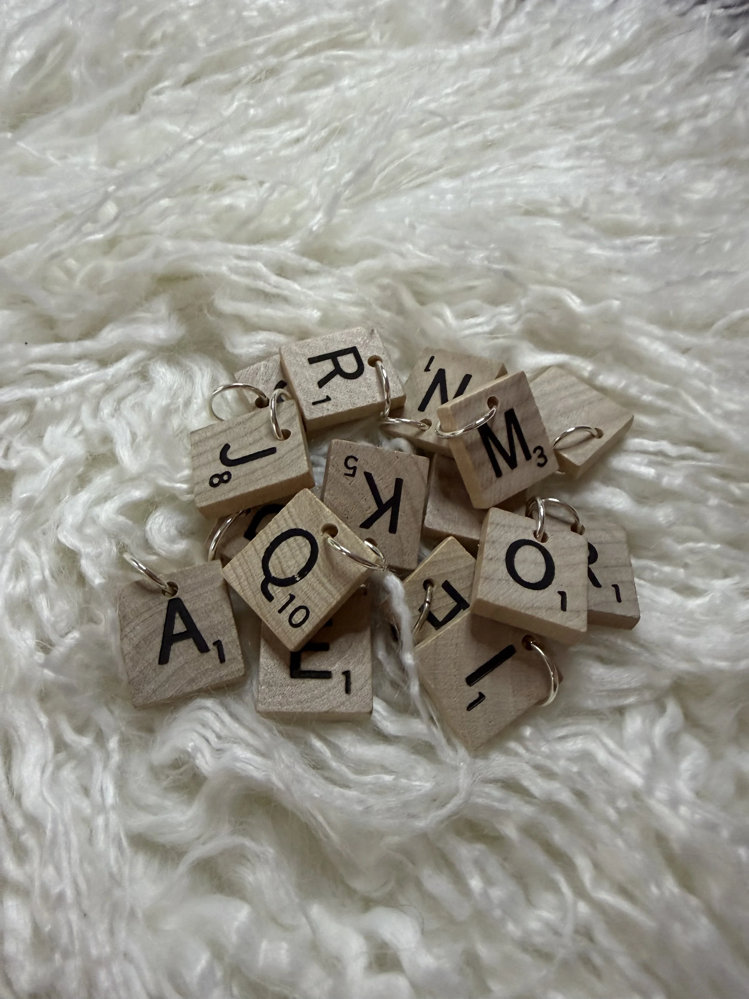 A pile of Scrabble tiles with letter rings placed on a fluffy white textured surface.