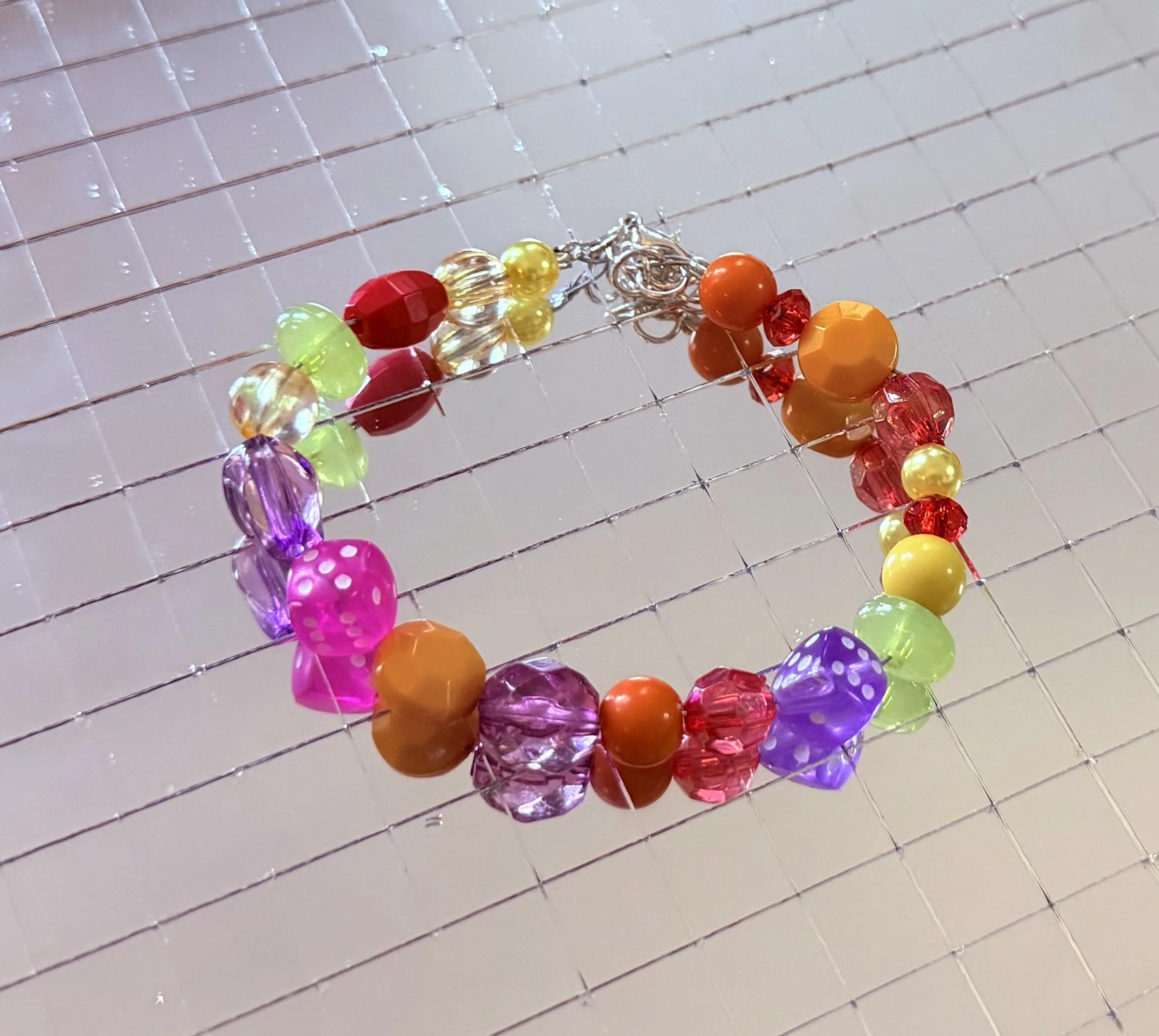Colorful beaded bracelet with various beads in red, orange, yellow, green, purple, and pink, placed on a metallic grid surface.