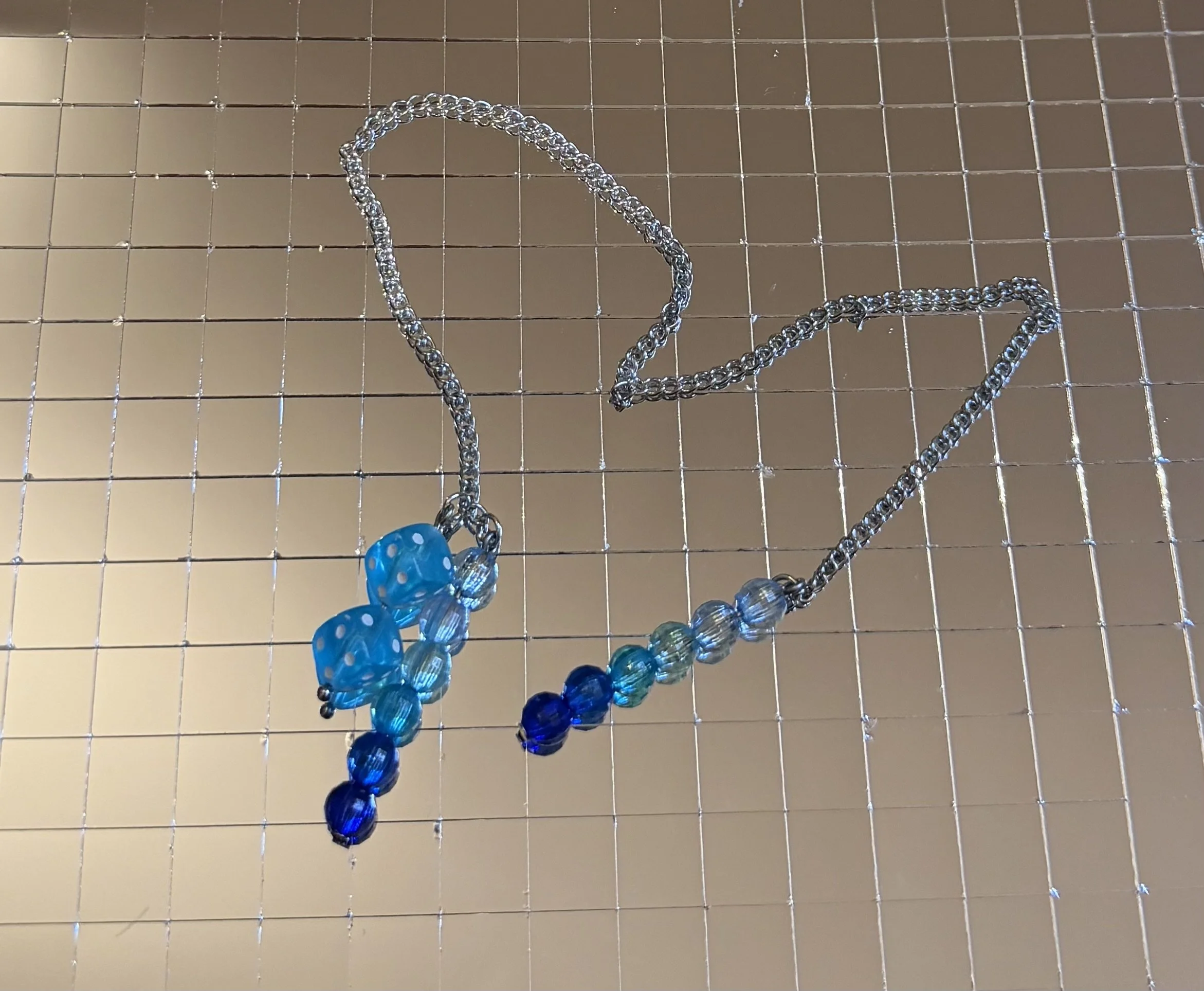 Colorful beaded necklace with blue and transparent beads hanging on a metal grid background.